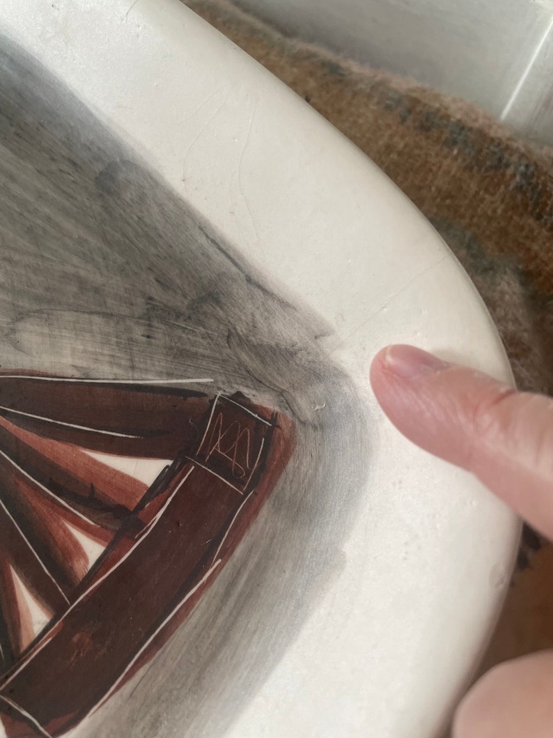 May include: A white ceramic plate with a brown and gray abstract design. The plate has a signature in the corner.