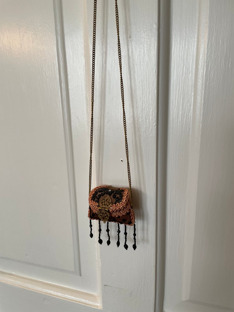 May include: A small, ornate, brown and black purse with a gold clasp and black beaded fringe hanging from a gold chain.