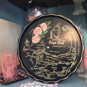Könnte beinhalten: Ein schwarzes Tablett aus Metall mit einer Karte von Cape Cod, Massachusetts. Die Karte zeigt die Städte und Gemeinden auf dem Kap, darunter Provincetown, Wellfleet, Chatham und Falmouth. Das Tablett hat auch einen goldenen Rand und eine goldene Inschrift mit der Aufschrift "Cape Cod, Massachusetts".