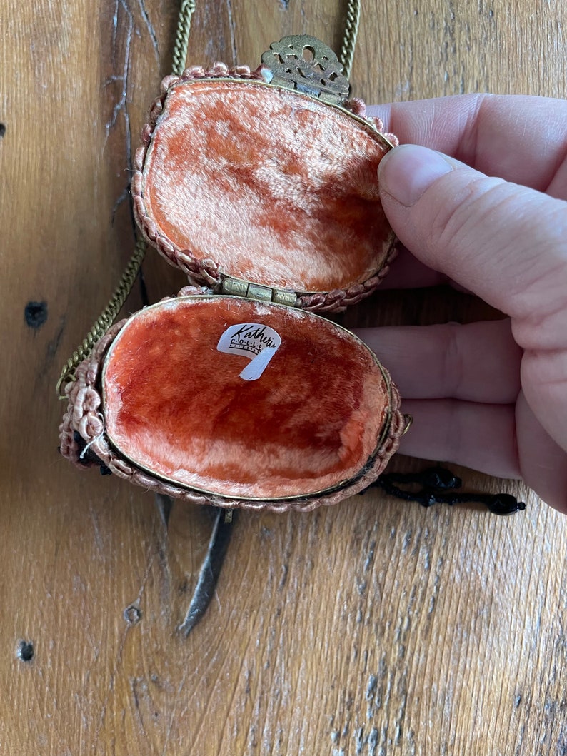 May include: A small, oval-shaped, beaded purse with a gold chain and clasp. The purse is open, revealing a red velvet lining and a label that reads "Kathy's Collectibles".