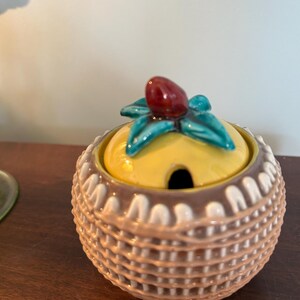 May include: A ceramic sugar bowl with a woven pattern in brown and white. The lid is yellow with a green leaf and red berry design.