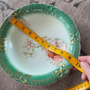 May include: A green and gold ceramic bowl with a floral design and the text "Mt. Clemens Mich. 1904". The bowl is 9 inches in diameter.