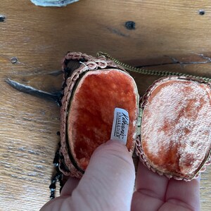 May include: A small, oval-shaped, beaded purse with a gold chain and a red velvet lining. The purse is open and the lining is visible. The label inside reads "Kathworth's - Exclusive Collection."