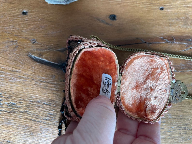 May include: A small, oval-shaped, beaded purse with a gold chain and a red velvet lining. The purse is open and the lining is visible. The label inside reads "Kathworth's - Exclusive Collection."