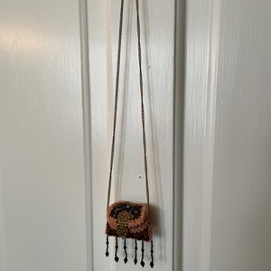 May include: A small, beaded, brown and black purse with a gold clasp and a long gold chain strap.