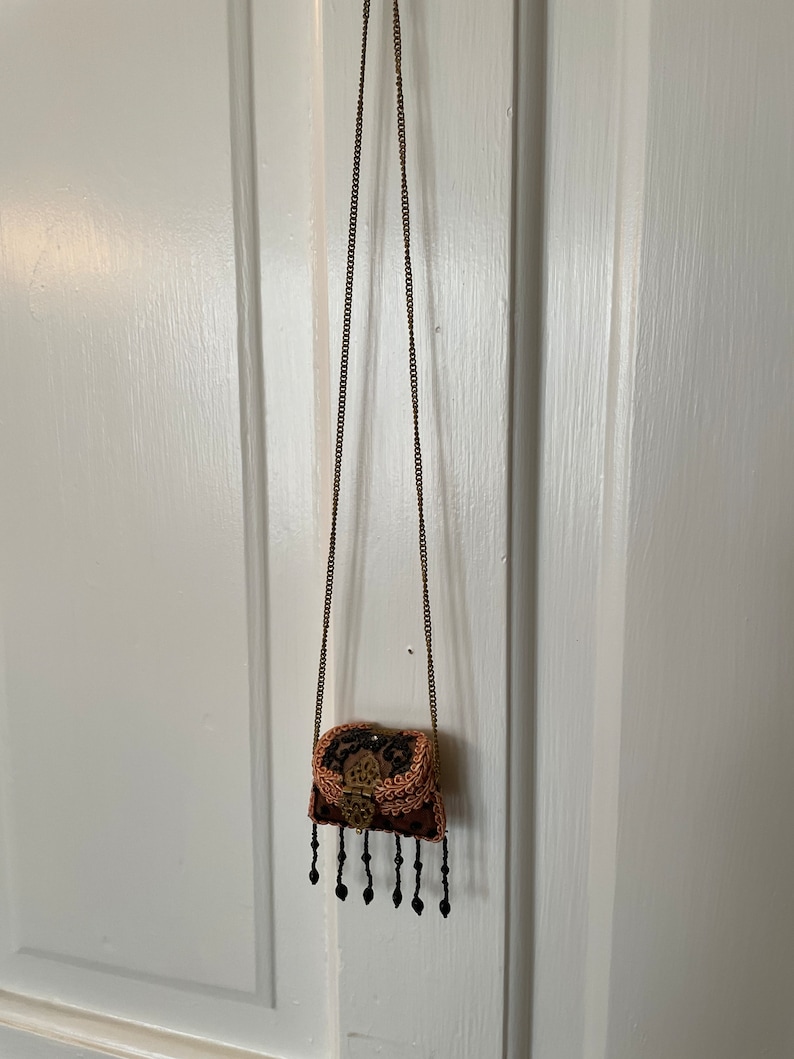 May include: A small, beaded, brown and black purse with a gold clasp and a long gold chain strap.