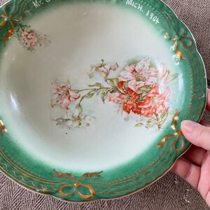 May include: A vintage green and white porcelain bowl with a floral design and gold trim. The bowl has the text "Mt. Clemens Mich. 1904" on the rim.