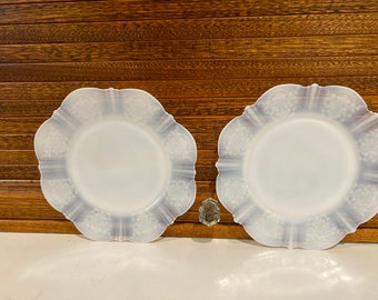 Könnte beinhalten: Zwei weiße Teller mit gewelltem Rand und einem zarten Blumenmuster in hellblau. Die Teller sind aus Milchglas und haben eine Vintage-Ästhetik.