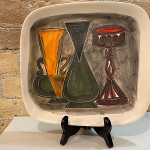 May include: A ceramic serving tray with a hand-painted design of three stylized vases. The vases are painted in shades of green, orange, brown, and black against a gray background.