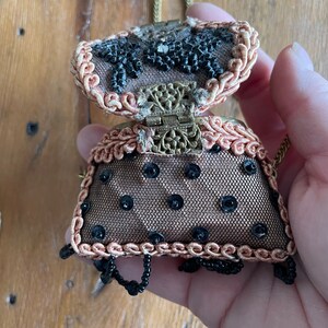 May include: A small, beaded purse with a gold chain and a black and brown design. The purse is open, revealing a black and gold interior.