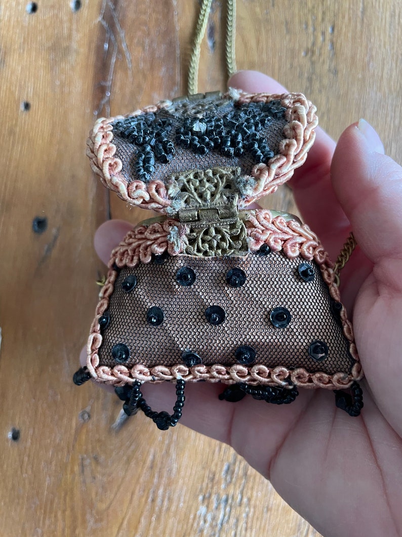 May include: A small, beaded purse with a gold chain and a black and brown design. The purse is open, revealing a black and gold interior.