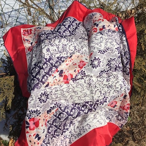 May include: A white silk scarf with a red border and a floral pattern in shades of pink, blue, and white.
