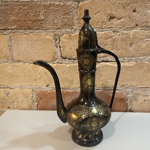 May include: A black metal teapot with gold floral designs. The teapot has a spout and a handle.