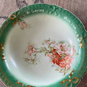 May include: A vintage green and white porcelain bowl with a floral design and gold trim. The bowl is inscribed with "Mt. Clemens Mich. 1904".