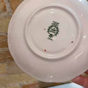May include: White ceramic saucer with a green and gold design that reads "Queen Anne Fine Bone China England" and "Noel..."