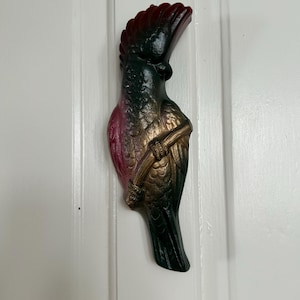 May include: A black, green, and gold painted bird figurine with a red crest. The bird is perched on a branch and has a detailed design.