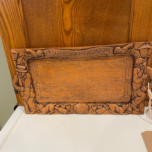 Puede incluir: Una bandeja de servir de madera con un diseño tallado de personas, animales y notas musicales. La bandeja es rectangular y tiene un acabado marrón.