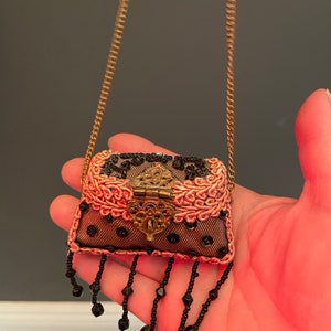 May include: A small, pink and black beaded purse with a gold chain strap. The purse has a decorative metal clasp and black bead fringe.