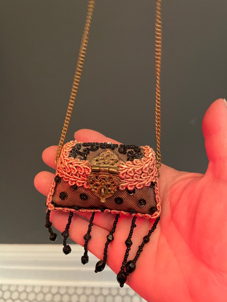 May include: A small, pink and black beaded purse with a gold chain strap. The purse has a decorative metal clasp and black bead fringe.