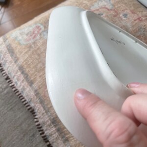 May include: White ceramic plate with a slightly curved edge. The plate has a small scratch on the surface.