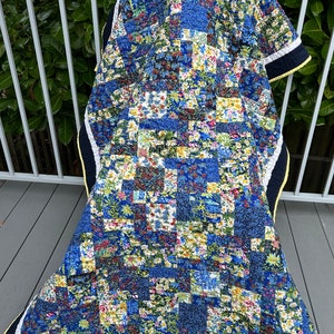 May include: A patchwork quilt with a floral pattern in shades of blue, white, and yellow. The quilt has a navy blue border with a yellow trim. The quilt is made of various fabric squares.