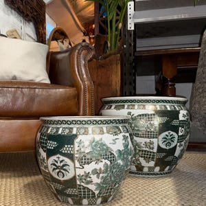 May include: Two round ceramic planters featuring a white base with intricate dark green and gold geometric patterns, floral motifs, and decorative borders. The planters have a wide, open top and a curved body, showcasing a detailed, multi-panel design.