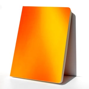 May include: A bright orange notebook with a gradient effect, transitioning from a darker orange to a lighter yellow. The notebook is closed and lying on a white surface.