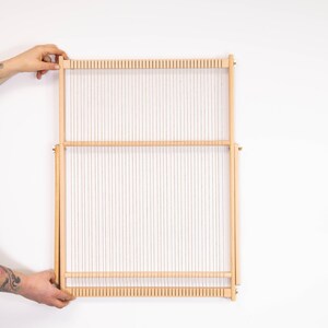 K&ouml;nnte beinhalten: Ein Webstuhl aus Holz mit wei&szlig;em Kettfaden, bereit zum Weben. Der Webstuhl ist aus Naturholz gefertigt und hat ein schlichtes Design.