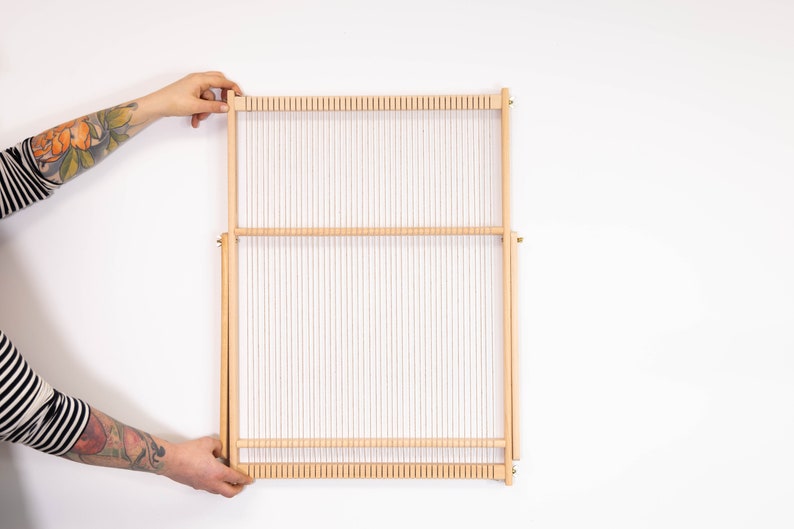 K&ouml;nnte beinhalten: Ein Webstuhl aus Holz mit wei&szlig;em Kettfaden, bereit zum Weben. Der Webstuhl ist aus Naturholz gefertigt und hat ein schlichtes Design.