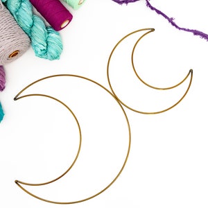 May include: Two gold metal crescent moon shapes on a white background.  There are several skeins of colorful yarn in the upper left corner of the image.