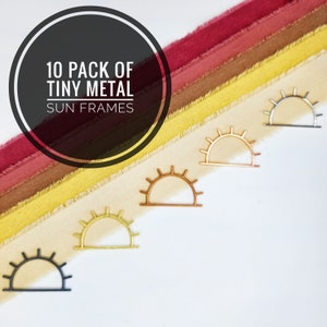 May include: A pack of 10 tiny metal sun frames in black, gold, and copper. The frames are arranged on a background of colorful fabric.