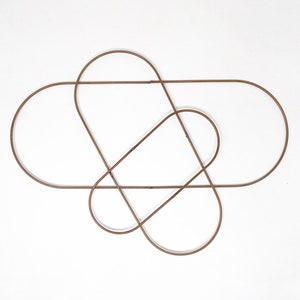 May include: A set of three interlocking metal hoops, each with a rounded top and bottom, creating a geometric design. The hoops are made of a light brown metal and are arranged in a symmetrical pattern.