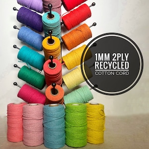 May include: A selection of 1mm 2-ply recycled cotton cord spools in various colours, displayed on a metal rack. The cord is available in colours such as pink, green, blue, yellow, and orange.