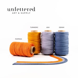 May include: Four spools of cotton cord in different colors: paprika, turmeric, ash, and denim. The spools are arranged in a row on a white surface.