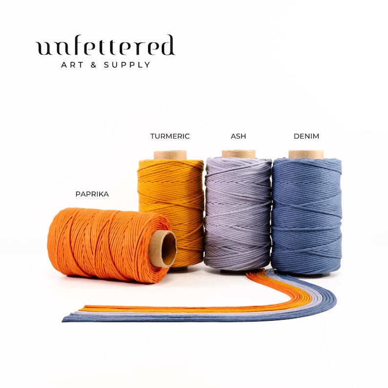 May include: Four spools of cotton cord in different colors: paprika, turmeric, ash, and denim. The spools are arranged in a row on a white surface.