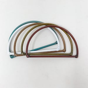 May include: Four metal hoops in different colours, stacked on top of each other. The hoops are teal, white, gold, and red.