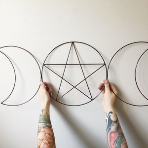 May include: A copper wire wall hanging with three circles, two crescent moons and a pentagram star in the center.