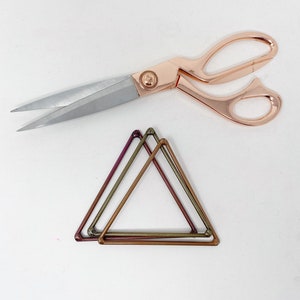 May include: Two overlapping metallic triangles in shades of green, purple, and copper. A pair of rose gold scissors are also in the image.
