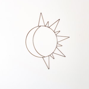 May include: A wire sculpture of a sun and moon, with the sun's rays extending out from the circle.
