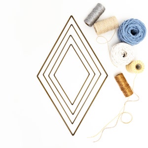 Peut inclure: Quatre bobines de ficelle de différentes couleurs et textures, dont beige, blanc, bleu et or, sont disposées autour d'un ensemble de quatre formes de diamants dorés concentriques.