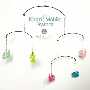 May include: A DIY kinetic mobile featuring snail cutouts in shades of green, pink, and blue. The mobile has black metal frames and hanging strings. The text "DIY Kinetic Mobile Frames" and "unlettered ART & SUPPLY" are visible.