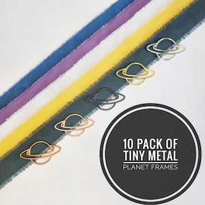 May include: Ten pack of tiny metal planet frames in gold, silver, black, and copper. The frames are arranged on a background of colorful fabric.