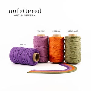 May include: Four spools of cotton cord in different colors: violet, thistle, paprika, and artichoke. The spools are arranged in a row on a white background. The text "unfettered art & supply" is at the top of the image.