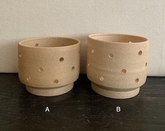 May include: Two beige ceramic planters with drainage holes. The planter on the left is labeled "A" and the planter on the right is labeled "B".