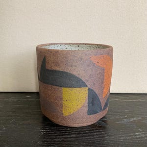 May include: A brown ceramic planter with a geometric design in black, orange, and yellow.