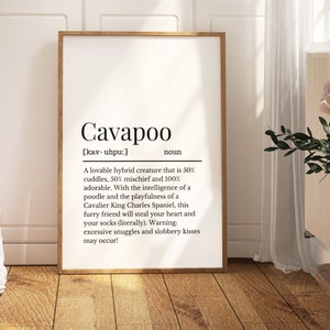 May include: A framed print featuring the definition of "Cavapoo" in black text on a white background. The definition describes the Cavapoo as a lovable hybrid dog. The frame is a light brown colour. The print is displayed indoors.