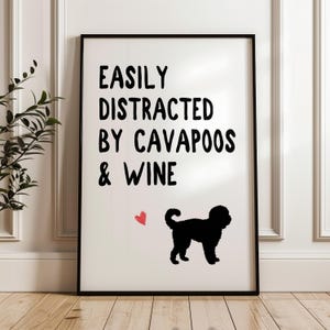 May include: A framed print with the text "EASILY DISTRACTED BY CAVAPOOS & WINE". The print features a black Cavapoo dog silhouette and a small red heart on a white background.