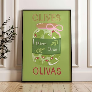May include: A framed art print depicting a jar of green olives with red highlights. The words "OLIVES" and "OLIVAS" are in red, with "Olives" and "Olivas" on a green label. A pink bow decorates the jar.