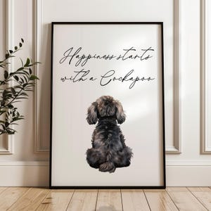 May include: Framed print with a Cockapoo illustration. The artwork shows a Cockapoo dog from the back, with the text "Happiness starts with a Cockapoo" in script. The print is set against a white backdrop and framed in black.