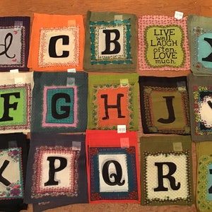 May include: A set of 26 colorful fabric squares with letters of the alphabet printed on them. Each square has a different pattern and design. The letter "X" is blue, the letter "Y" is white, and the letter "Z" is green. The squares are arranged in rows and columns. The text "LIVE well, LAUGH often, LOVE much." is printed on one of the squares.